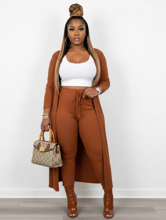 Woman wearing a brown ribbed outfit with a white top, holding a handbag on a white background